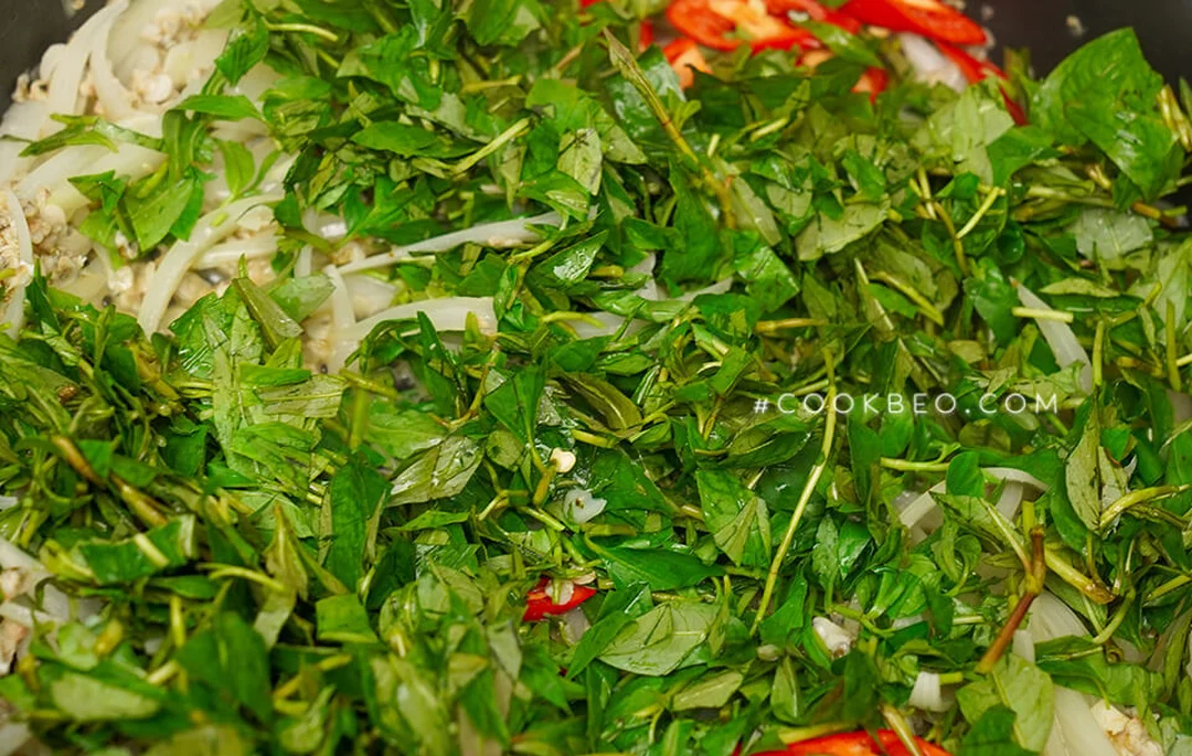 hến xào xúc bánh đa với rau răm được đảo nhanh trên chảo